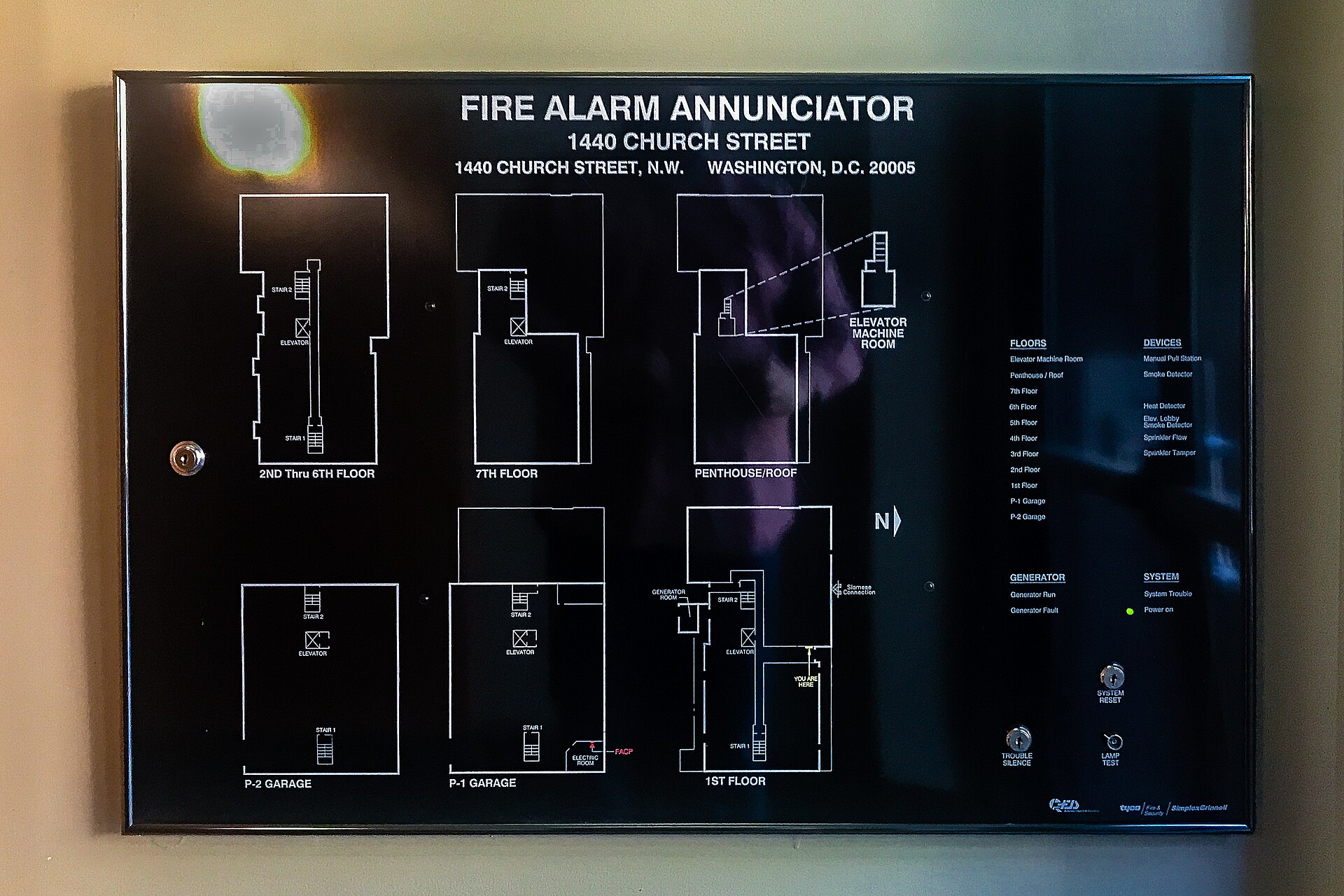 A fire alarm annunciator panel in a lobby: a black board printed with the white floor plans of every level, each one labelled.
